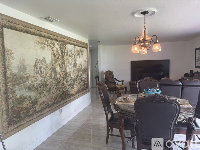 A dining room with a large painting on the wall and a chandelier hanging from the ceiling.