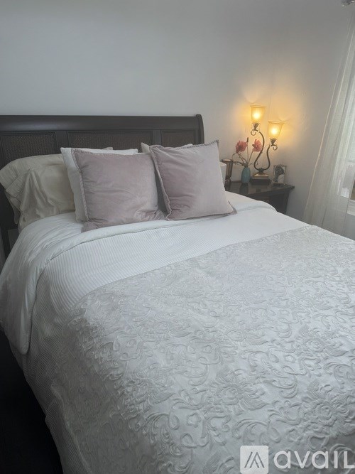 A bed with a white comforter and two pillows sits in a room with a lamp on a side table.