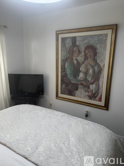 A bedroom with a bed, a television, and a framed picture on the wall.