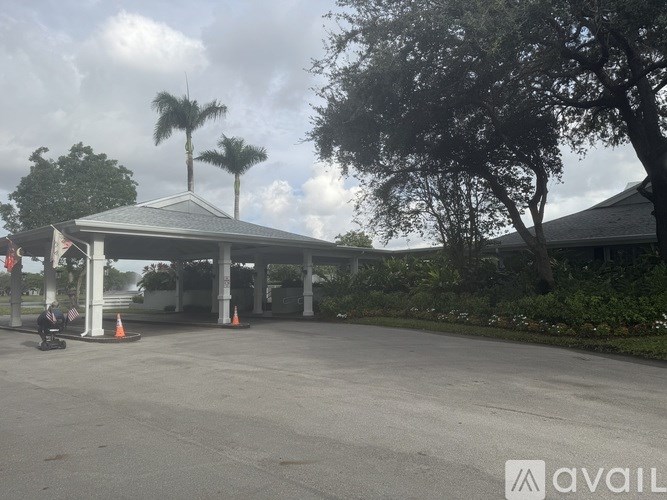 A person is sitting on a bench under a pavilion with trees in the background.