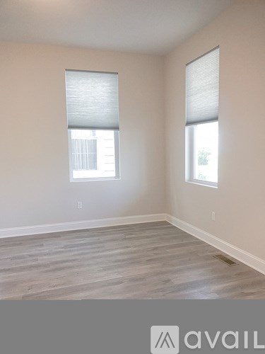 A room with wooden flooring and two windows.