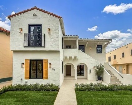 A white house with a black balcony and wooden shutters.