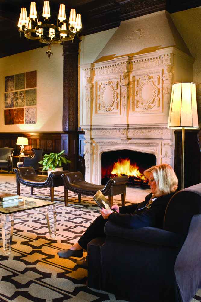 a woman sitting in a chair reading a magazine in front of a fireplace