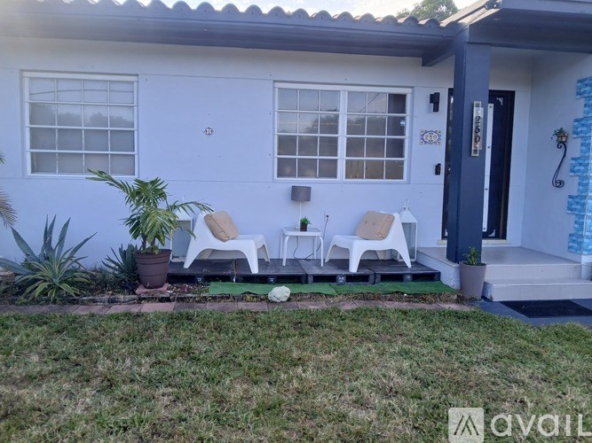 A white house with a blue door and two white chairs.