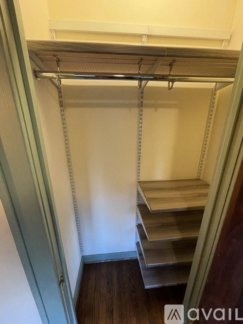 A white shelving unit with a grey metal frame and a white top is in a room with a white wall and a wooden floor.
