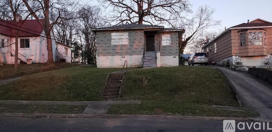 A small house with a red roof is situated on a grassy area next to a road.