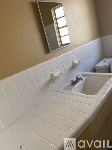 A bathroom with a white tiled sink and a mirror above it.