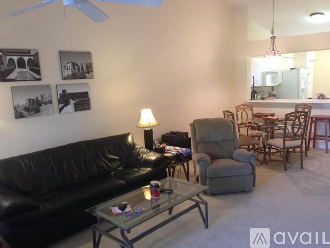 A living room with a black leather couch, a glass coffee table, and a ceiling fan.