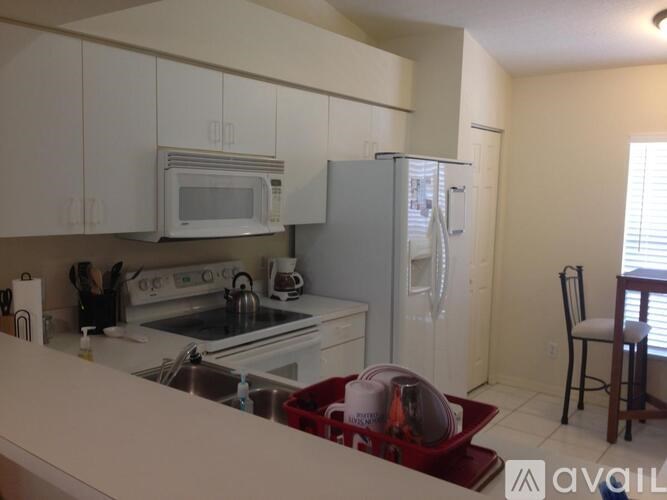 A kitchen with white cabinets and appliances, a red tray on the counter, and a window with blinds.