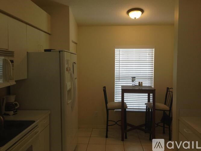 A kitchen with a refrigerator, a table with two chairs, and a window with blinds.