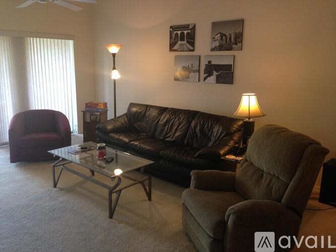 A living room with a black couch, a brown chair, and a glass coffee table.