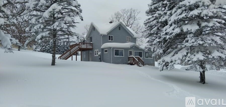 A house with a grey roof and a balcony is surrounded by snow-covered trees.