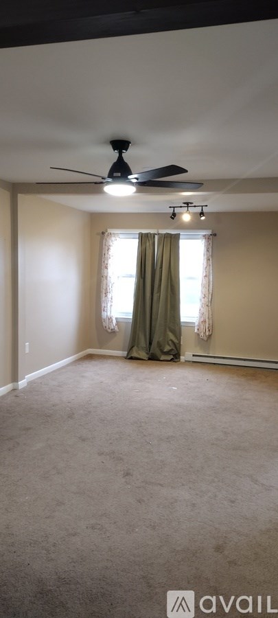 A room with a ceiling fan and a window with curtains.