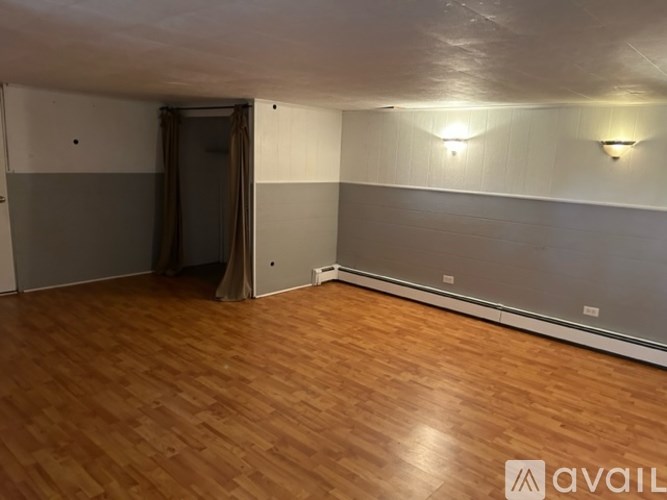 A room with wooden flooring and a grey wall with a brown curtain.