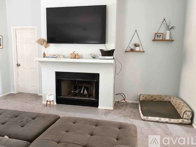 A living room with a fireplace, grey ottoman, and a television mounted on the wall.