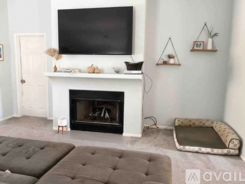 A living room with a fireplace, grey ottoman, and a television mounted on the wall.