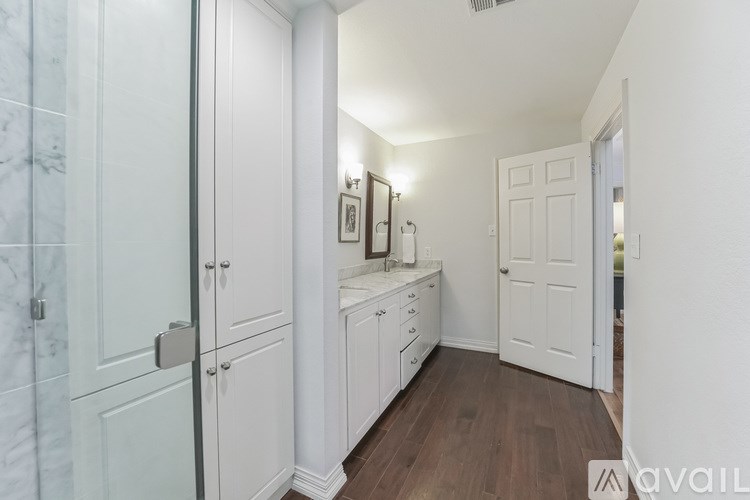 A white bathroom with a marble tile wall and a wooden floor.