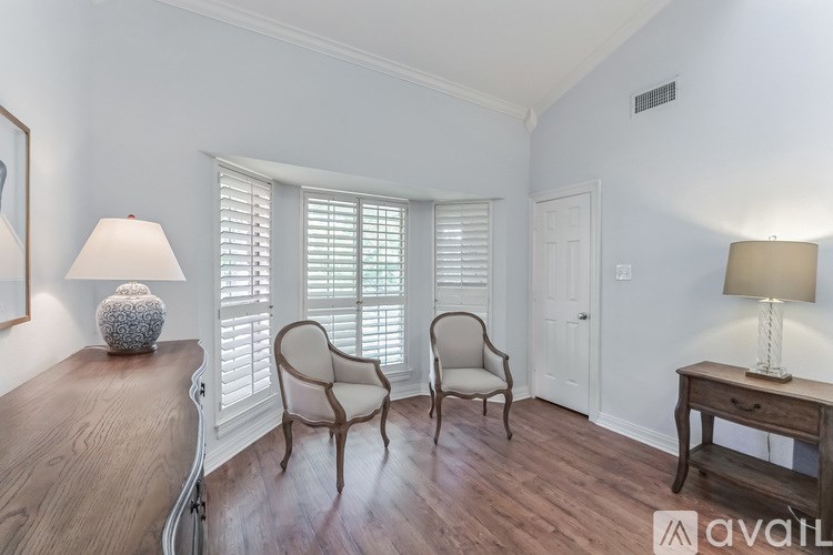 A room with a wooden floor, two chairs, a table with a lamp, and a painting on the wall.