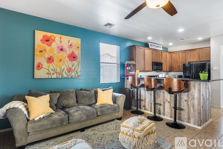A living room with a couch, a rug, a ceiling fan, and a kitchen area in the background.