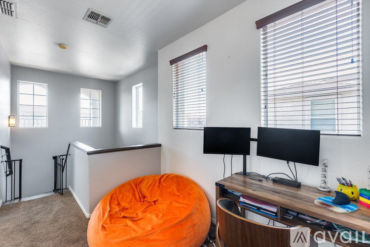 A room with a desk, two monitors, and an orange bean bag chair.