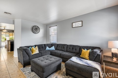 A living room with a grey couch and a clock on the wall.