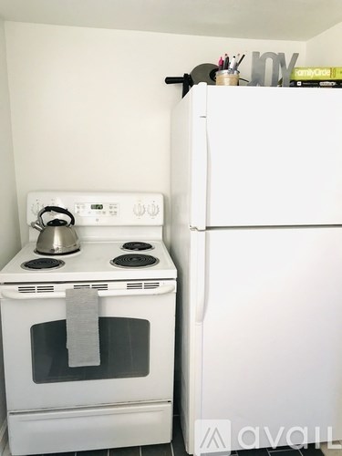 A white oven with a kettle on top and a white fridge in a kitchen.