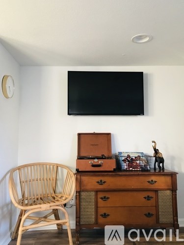 A wooden chair is placed in front of a brown chest of drawers with a black television mounted on the wall above it.