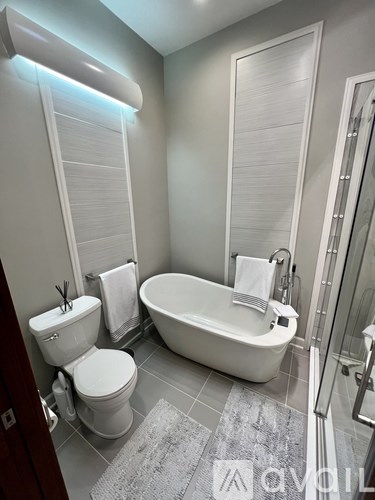 A white toilet and bathtub in a bathroom with a grey rug.