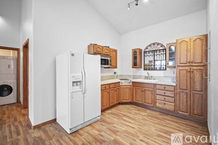 A kitchen with wooden floors and cabinets, a white refrigerator, and a window.