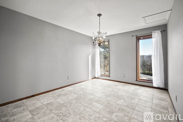 A spacious room with a chandelier, large windows with curtains, and a tiled floor.