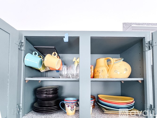 A cabinet with two shelves, one with blue and yellow cups and the other with yellow and orange dishes.