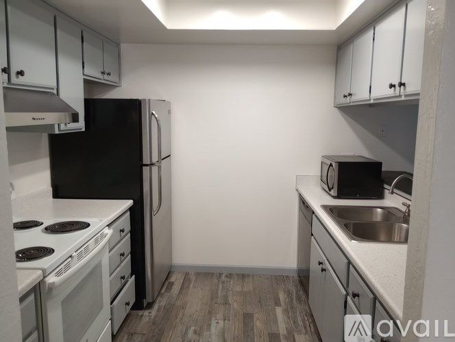 A kitchen with a black refrigerator, white countertops, and wooden flooring.