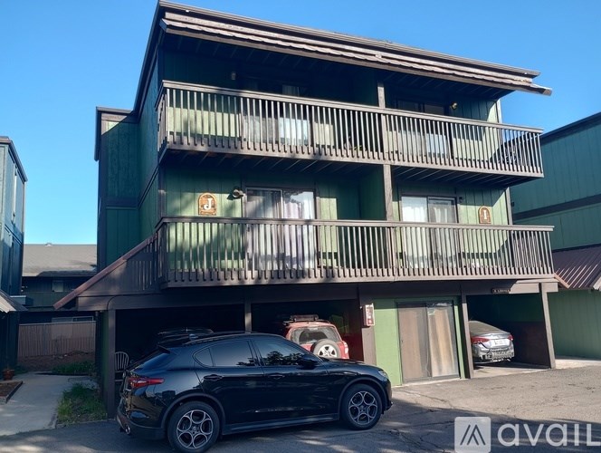 A black car is parked in front of a green building with a balcony.