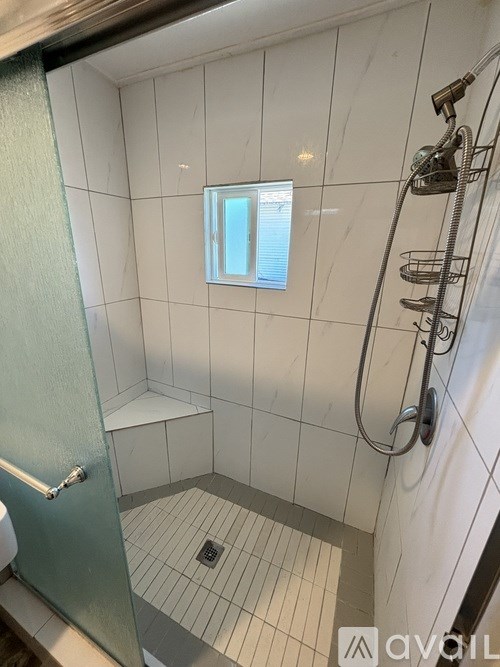 A white tiled bathroom with a glass shower door and a window.