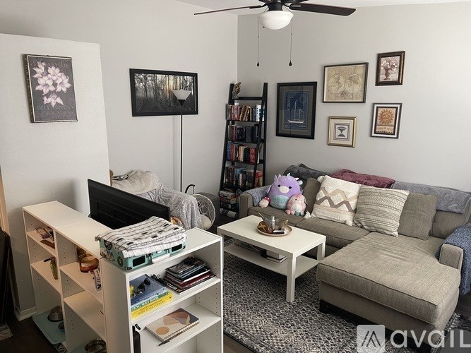 A living room with a grey couch, a white coffee table, a bookshelf, and a ceiling fan.