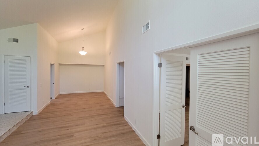 A room with wooden floors and white walls, with a hanging light fixture and a door with a closed shutter.