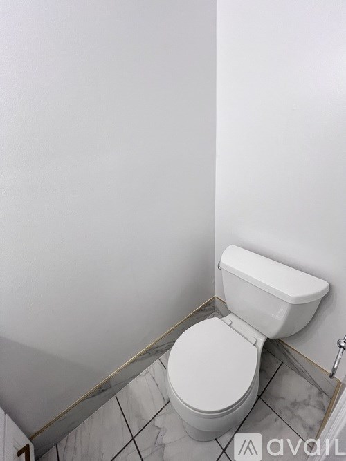 A white toilet with a white tank is in a bathroom with white walls.