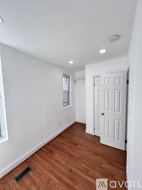 A room with a white door and a window with white walls and wooden flooring.