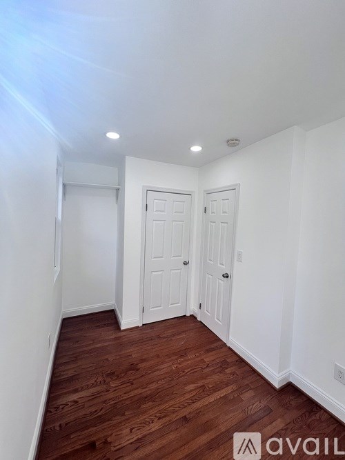 A room with wooden floors and white walls, with two doors and a window.