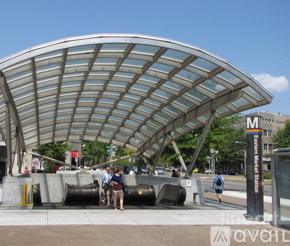 A curved glass and metal structure provides shade for a group of people standing underneath it.