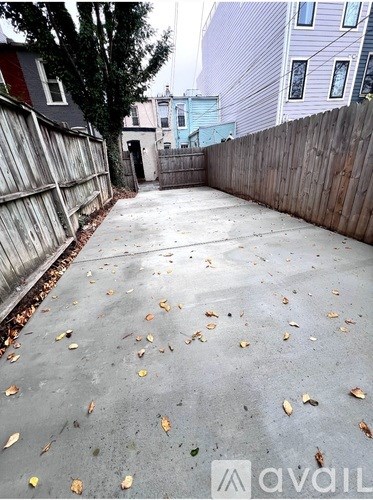 A backyard with a concrete ground and fallen leaves.