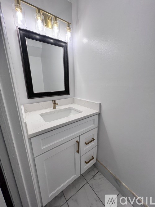 A bathroom with a white sink and a mirror with lights above it.