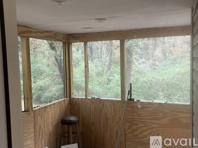 A room with wooden walls and a window overlooking a forest.