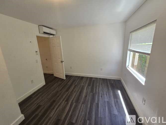A room with a wooden floor and a door leading to another room.