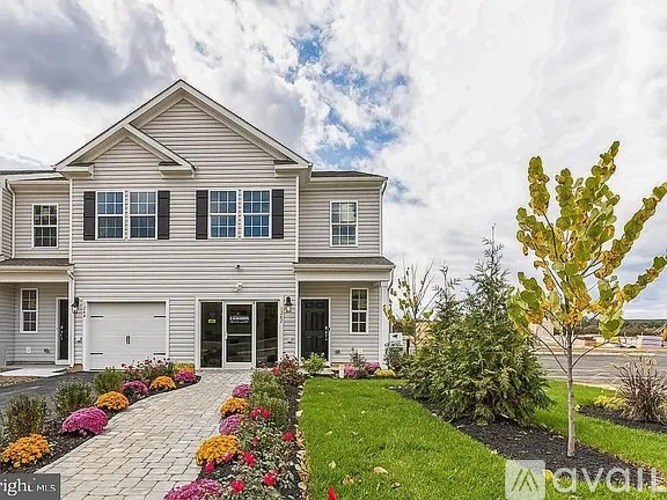 A house with a grey siding and a white garage door is surrounded by a garden with a variety of colorful flowers.