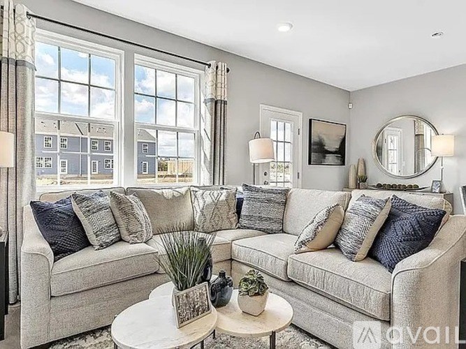 A living room with a large window, a grey couch, and a white coffee table.