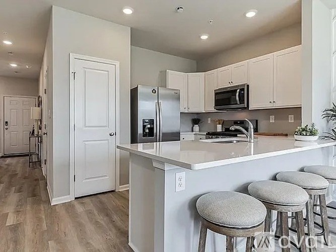 A kitchen with white cabinets and a white island with four stools.