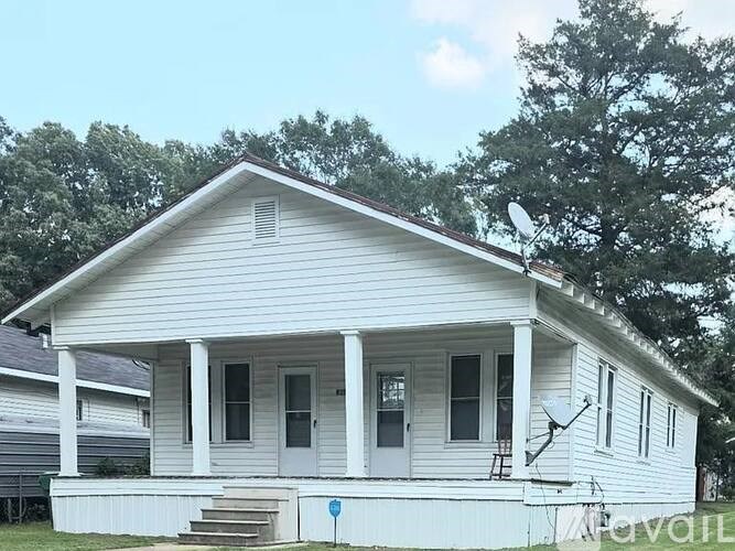 A white house with a porch and a satellite dish on the roof.