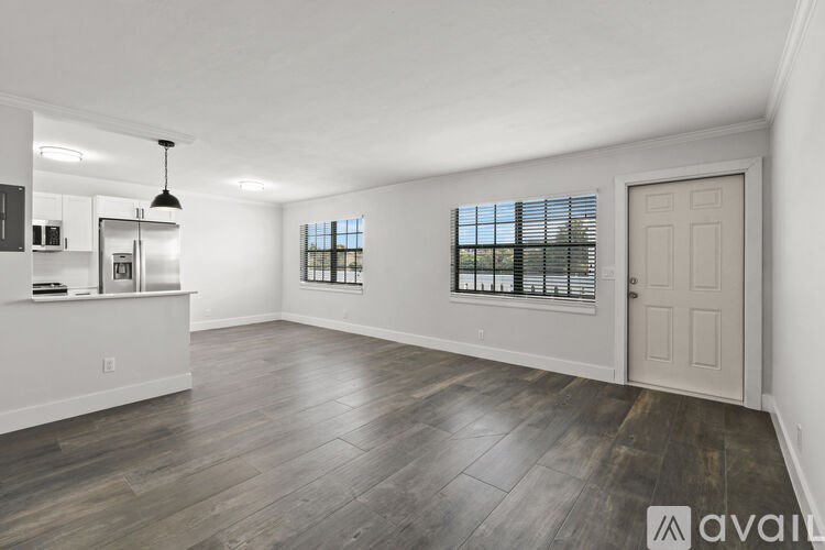 A spacious room with wooden flooring and a large window with blinds.