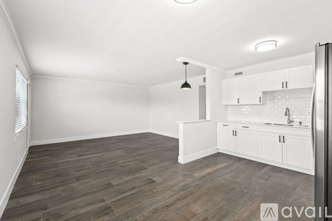 A kitchen area with white cabinets and a wooden floor.